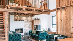 Un loft espacioso con techo alto, vigas de madera a la vista, una escalera empotrada y una zona de estar acogedora con sofás cómodos y una mesa de centro.