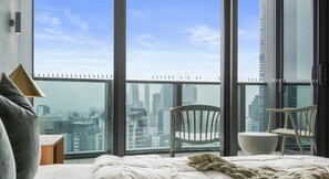 A bedroom with a large window, a bed, a chair, and a small table. - Facehome QWR (Brisbane)