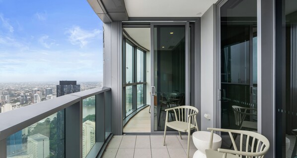 A balcony with a view of the city, a glass door, and two white chairs. - Facehome QWR (Brisbane)