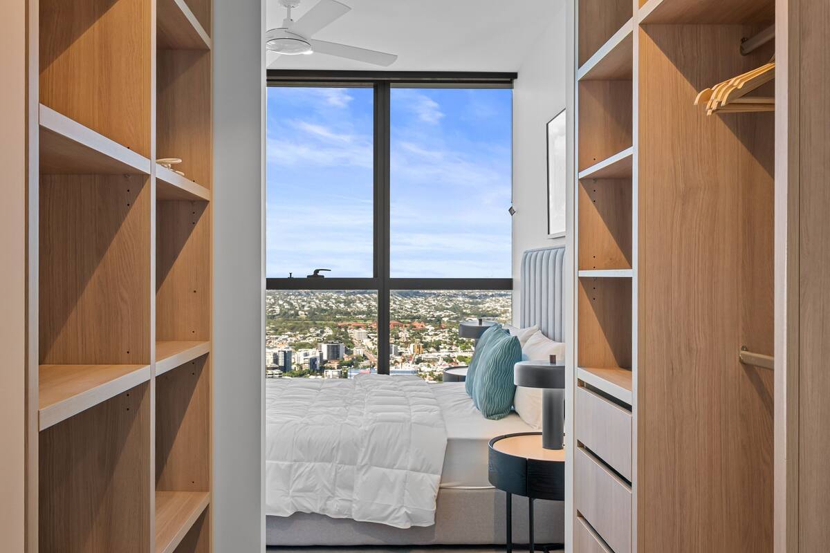 Ein Schlafzimmer mit Blick auf die Stadt, ein Bett, ein Nachttisch und eingebaute Holzregale.