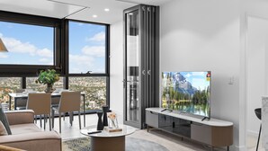 A modern living room with a dining area, large windows, a TV, and a view of a mountain lake. - Facehome QWR (Brisbane)