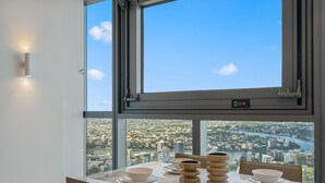 A dining table with white plates and bowls, a wooden centerpiece, and a view of a cityscape through a large window. - Facehome QWR (Brisbane)