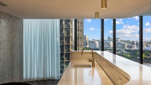 A modern bathroom with a curved vanity, a gold faucet, and a large window offering a city view. - Facehome QWR (Brisbane)