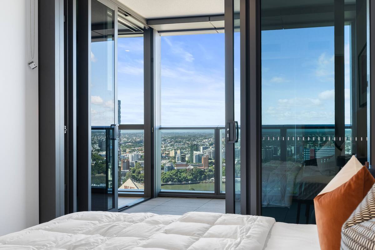 Ein modernes Schlafzimmer mit einem großen Bett, Blick auf die Stadt durch raumhohe Fenster und einem Balkon.