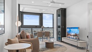 A modern living room with a large window, a ceiling fan, a flat-screen TV, and a dining area with chairs and a table. - Facehome QWR (Brisbane)