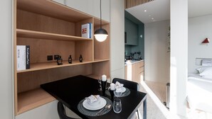 A modern hotel room with a dining area, a kitchenette, and a bed.