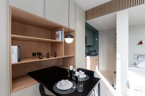 A modern hotel room with a dining area, a kitchenette, and a bed.