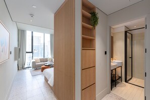Een moderne hotelkamer met een groot raam, een bed, een houten scheidingswand, een klein tafeltje met een plant en een douchecabine met glazen wanden.