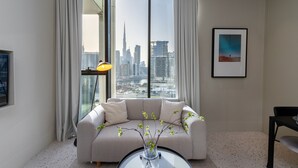 A modern living room with a large window offering a city view, a sofa, a coffee table with a vase, and a framed picture on the wall.