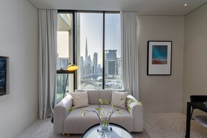 Una sala de estar moderna con un ventanal que ofrece vistas a la ciudad, un sofá, una mesa de centro con un florero y un cuadro enmarcado en la pared.