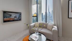 Een moderne woonkamer met een groot raam, een bank, een bijzettafeltje met een vaas en een flatscreen tv aan de muur.