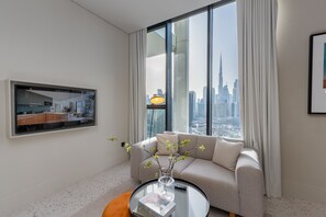 A modern living room with a large window, a sofa, a coffee table with a vase, and a flat-screen TV mounted on the wall.