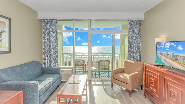 A living room with a sofa, armchair, coffee table, and TV on a wooden cabinet. - Oceanfront w/ Indoor Waterparks at Dunes Village! (Myrtle Beach)
