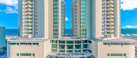 A high-rise hotel with multiple balconies, a central atrium, and a pool area.