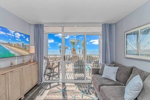 Ein Balkon mit Blick auf Strand und Meer, eine Couch, ein Fernseher und eine Essecke.
