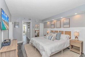 A bedroom with a large bed, bedside tables, a TV, and a view of the outdoors. - Luxe Oceanfront @ Seawatch Resort! (Horry County)