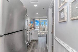 A kitchen with a stainless steel refrigerator, a built-in oven, and a window leading to a balcony with outdoor furniture. - Luxe Oceanfront @ Seawatch Resort! (Horry County)
