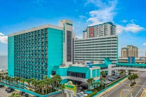 A hotel with a large building featuring a grid-like facade, a prominent sign, and a view of the ocean.