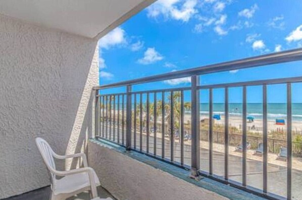 A balcony with a view of the beach, a white chair, and a metal railing.