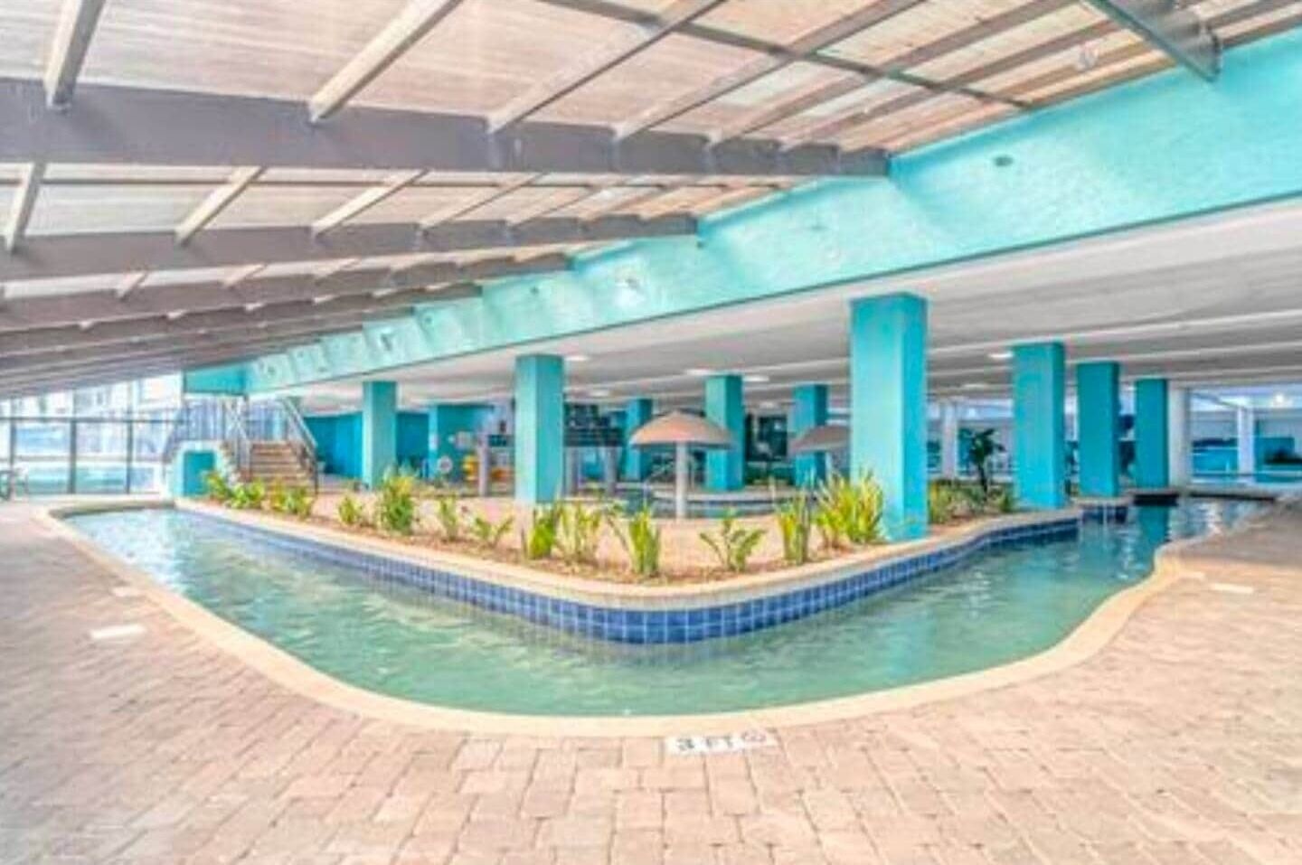 Una piscina interior con borde de azulejos, zona cubierta con techo y suelo de ladrillo.