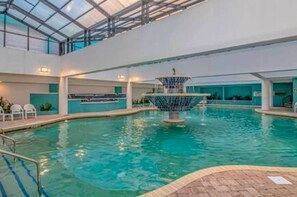 An indoor swimming pool with a central fountain, surrounded by seating areas and a glass ceiling. - Direct Oceanfront 1BR w/ lots of Pools! (Myrtle Beach)