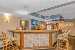 A bar area with wicker chairs, a counter, and a television screen. - Direct Oceanfront 1BR w/ lots of Pools! (Myrtle Beach)