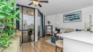 Un apartamento moderno con cocina, comedor y sala de estar. Cuenta con un ventilador de techo, un ventanal con vista a la ciudad y una mesa de comedor con sillas.