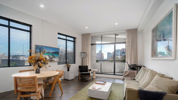 A modern living room with a dining area, large windows, a sofa, and a view of the city.