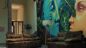 A room with two brown sofas, a lamp on a tripod, and a large mural on the wall. - El Pinche Hostal (Guadalajara)