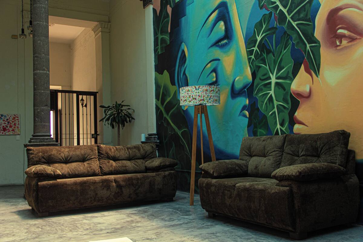 A room with two brown sofas, a lamp on a tripod, and a large mural on the wall.