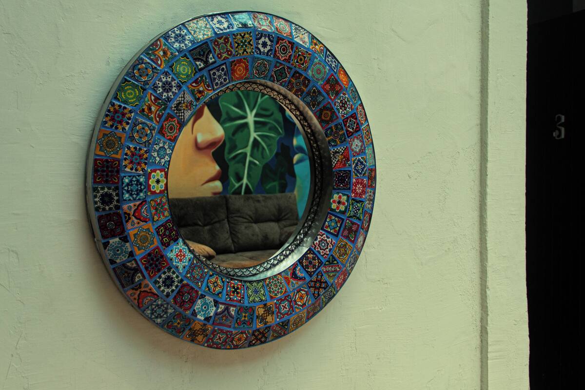 A circular mirror with a mosaic border on a wall.