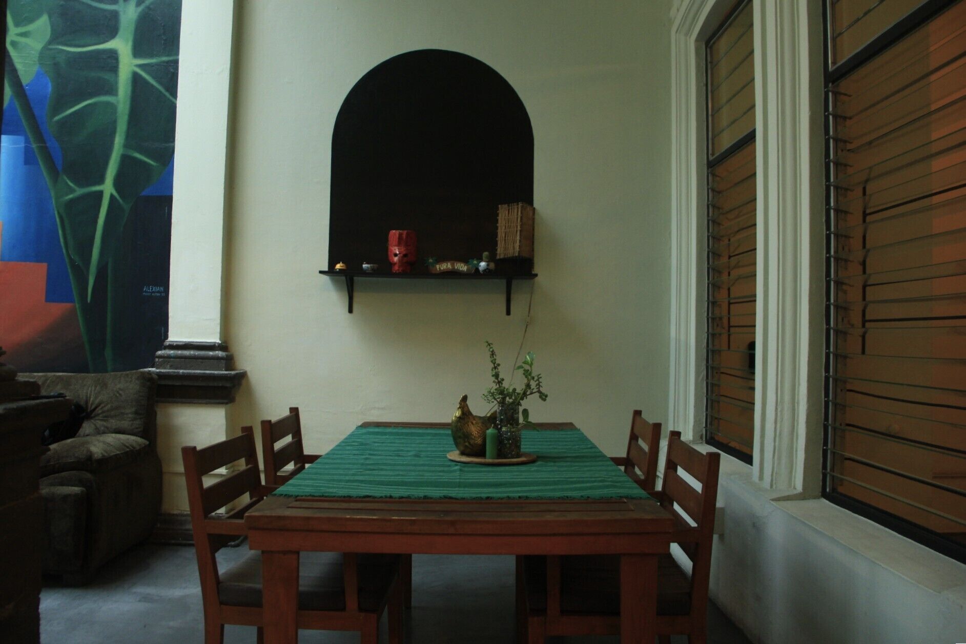 A dining area with a wooden table, green tablecloth, and four chairs. A decorative plant is on the table.