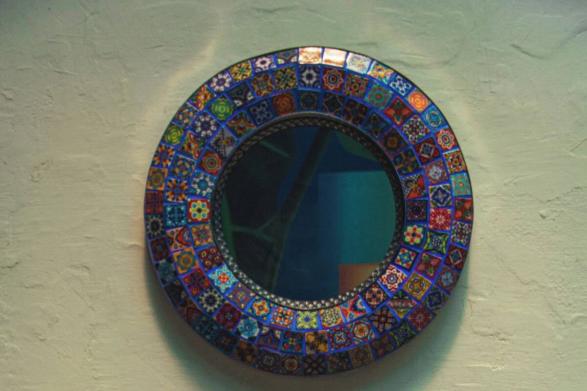 A mosaic mirror on a wall with a potted plant below it.