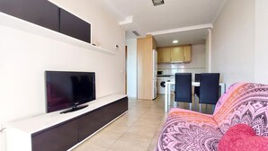 A modern living room with a flat-screen TV, a sofa, and a dining area with chairs.