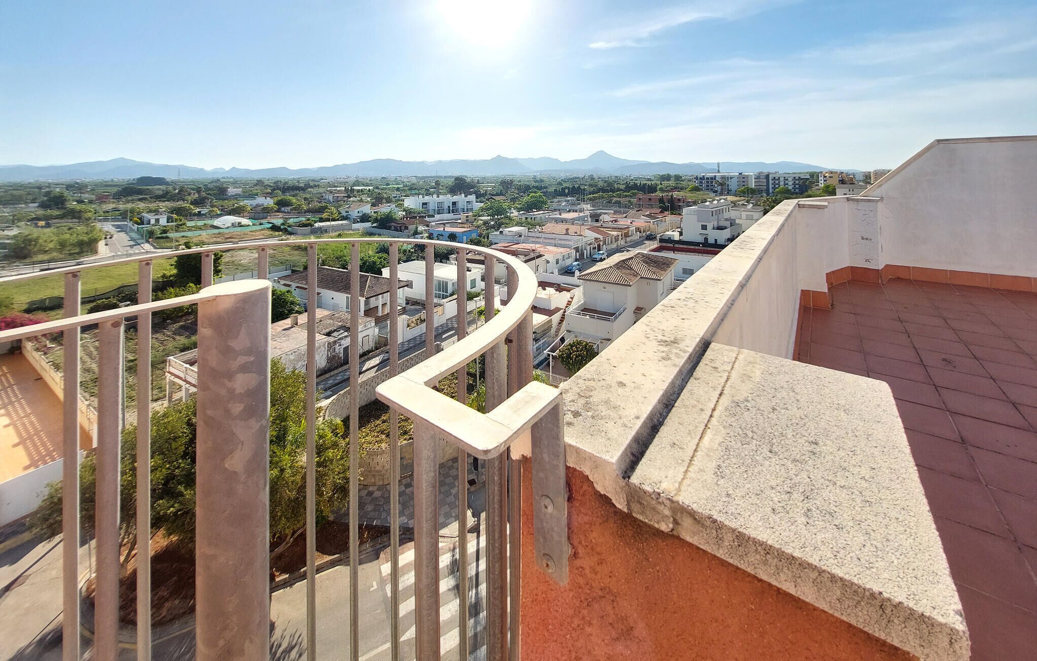 Un immeuble de grande hauteur doté d’un balcon offrant une vue sur le paysage urbain et les montagnes lointaines.