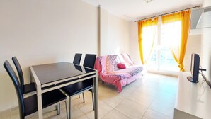 A dining area with a table and chairs, a sofa with a patterned blanket, and a TV on a stand.