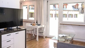 A modern room with a flat-screen TV, a dining table with chairs, a glass coffee table, and a sofa.