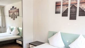 A hotel room with a bed, a bedside table, a nightstand, a mirror, and artwork on the wall.