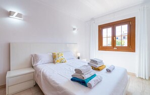 A hotel room with a bed, a nightstand, a window with curtains, and a wall-mounted light fixture.