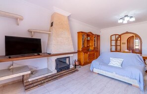 A room with a flat-screen TV, a fireplace, a wooden cabinet, and a bed.
