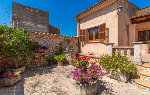 A courtyard with stone walls, potted plants, and a building with wooden shutters.