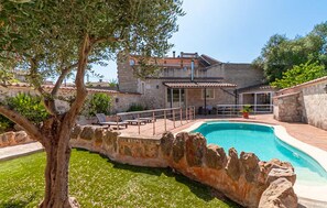 A stone villa with a swimming pool, outdoor seating, and a view of the surrounding landscape.