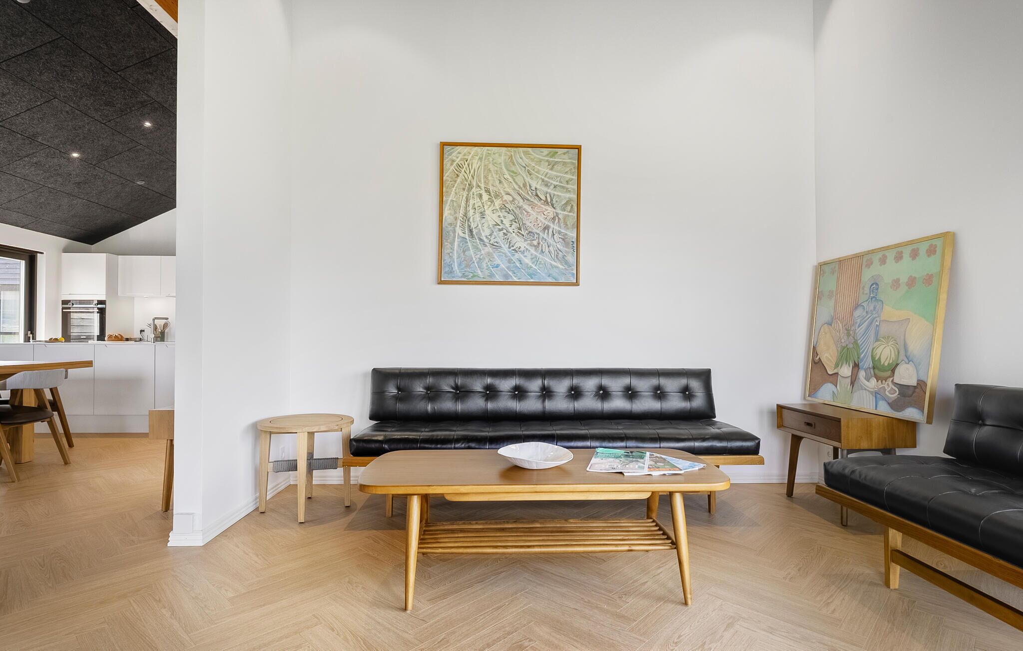 Una sala moderna con un sofá de cuero negro, una mesa de centro de madera y un comedor con mesa y sillas de madera.