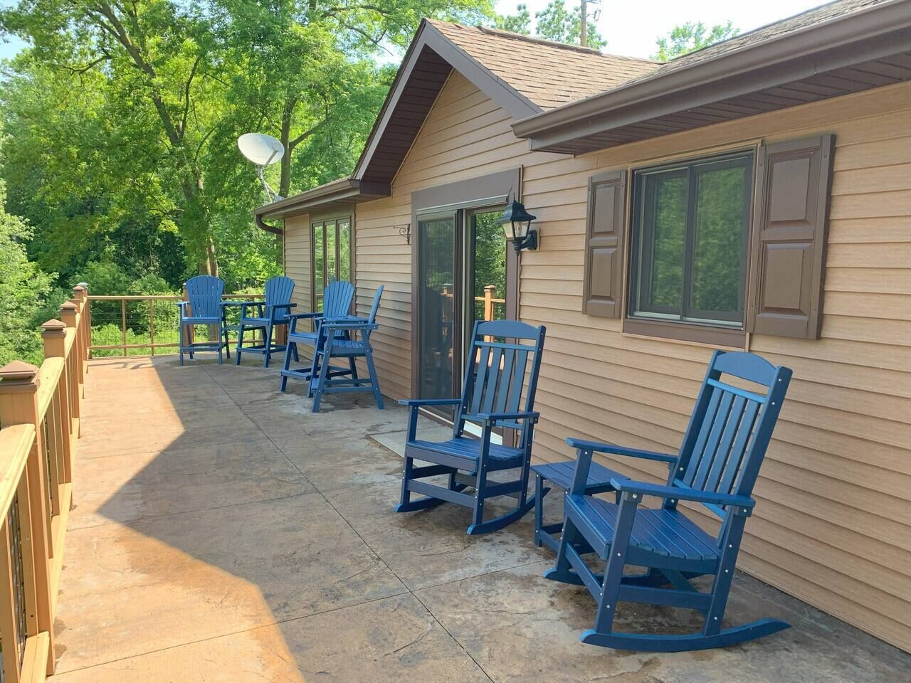 Een overdekt terras met blauwe Adirondack-stoelen en een schotelantenne.