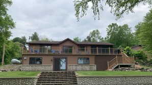A two-story house with a stone retaining wall, a wooden deck, and a staircase leading to a balcony.
