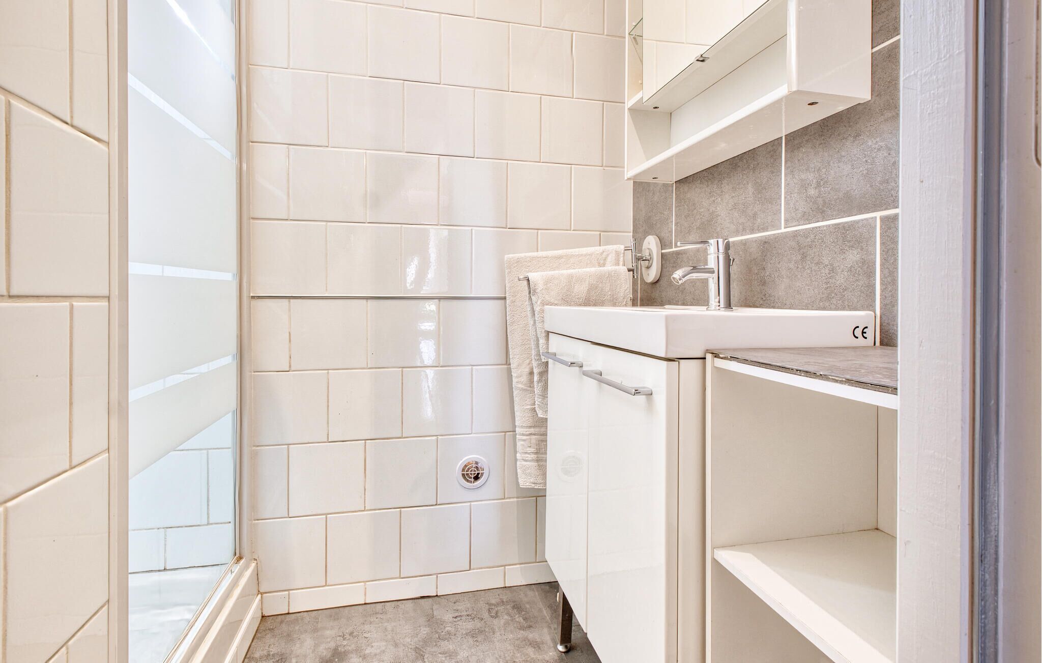A small, modern bathroom with white tiles, a shower, a sink, and a toilet.