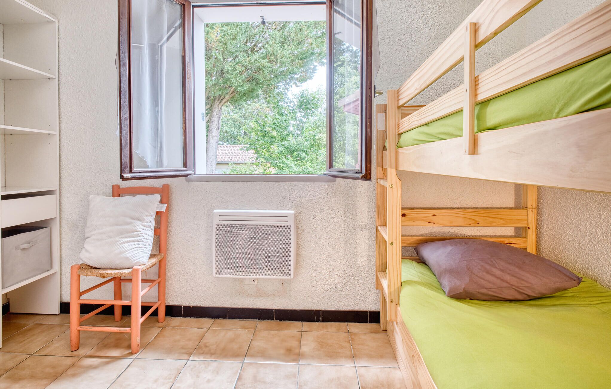 Een slaapkamer met een stapelbed, een raam, een radiator en een stoel.