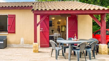 An outdoor patio with a round table and chairs, a red pergola, and a red car parked nearby.