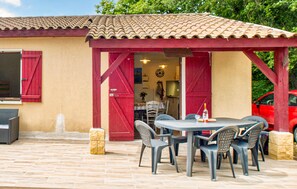 An outdoor patio with a round table and chairs, a red pergola, and a red car parked nearby.