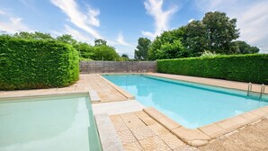 Una piscina rectangular con solárium de baldosas y una valla de madera al fondo.